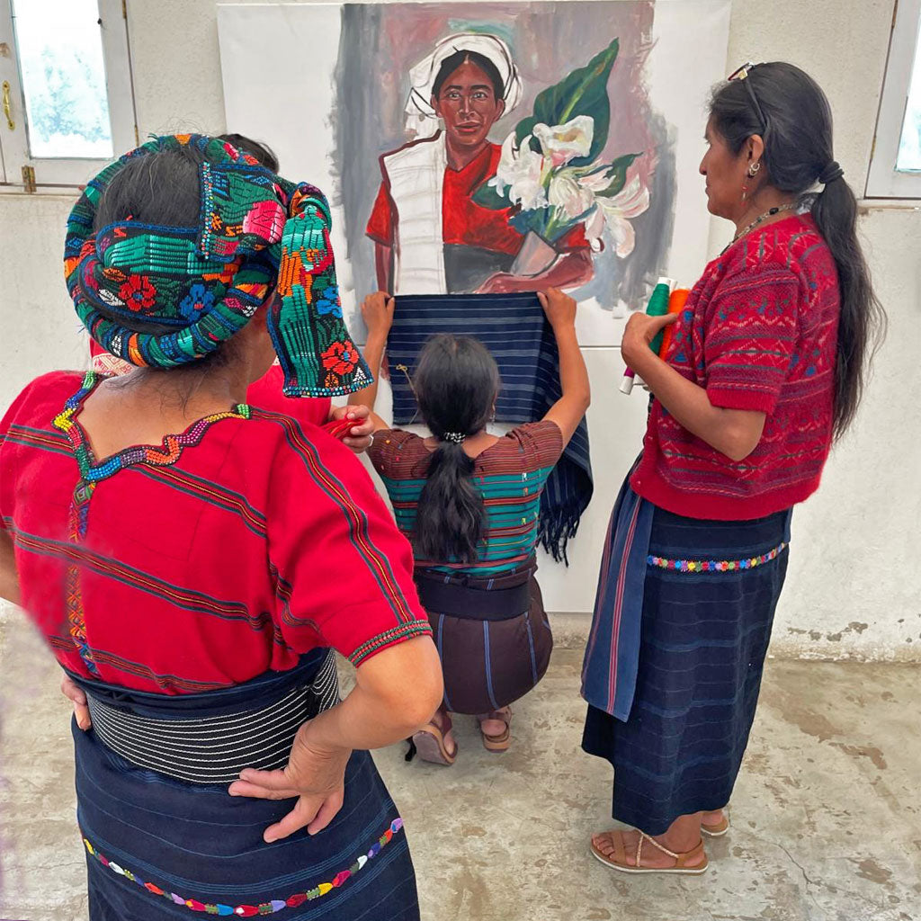three Mayan women dressed in traditional blouses and skirts working on a painting